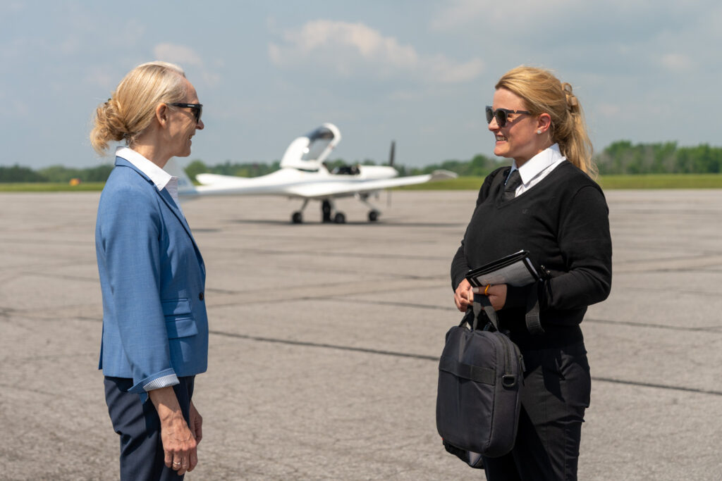Instructor and trainee standing beside a small training aircraft on the airport apron

