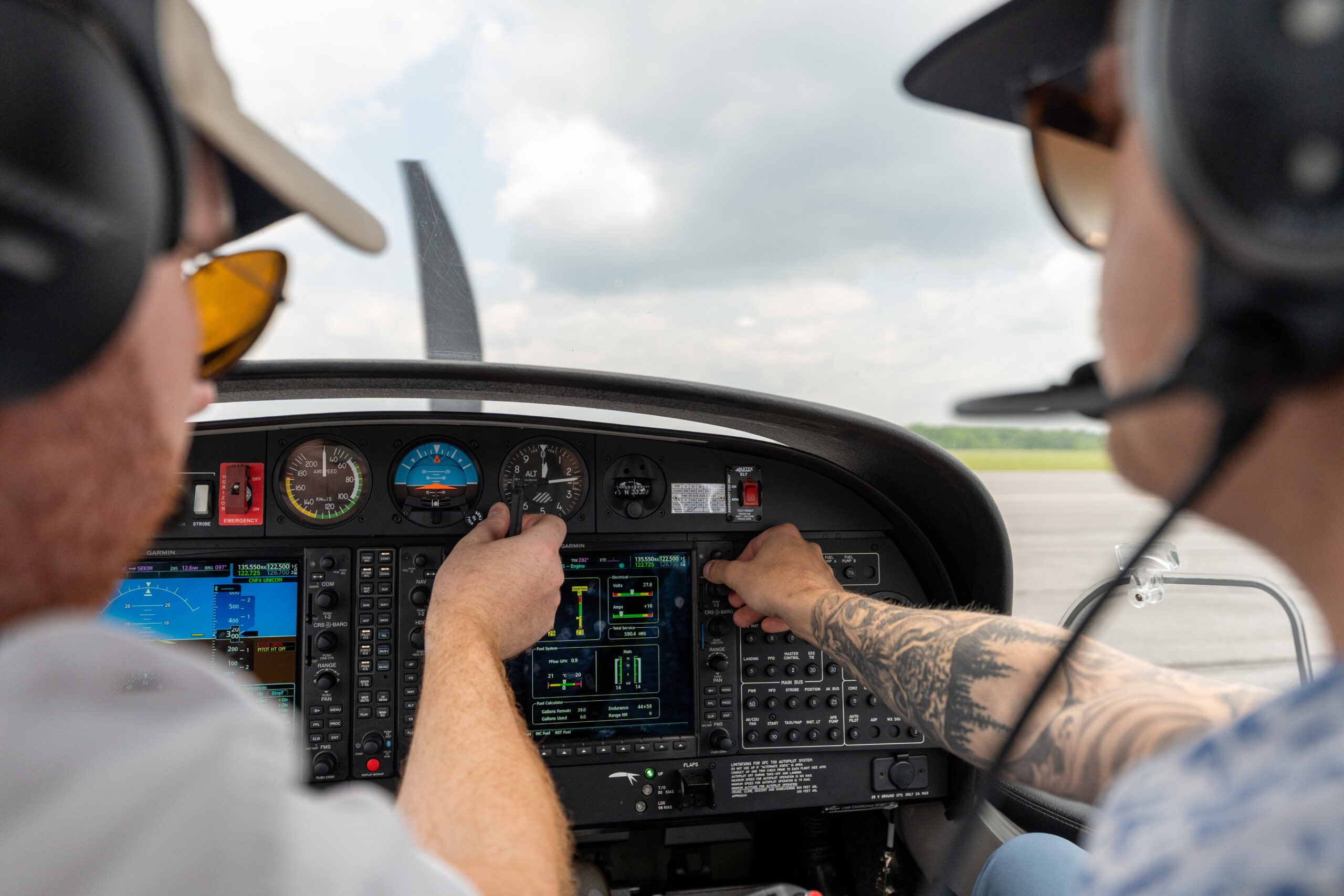 Two flight trainees seated in a small aircraft cockpit, pointing at flight instruments during hands‑on training