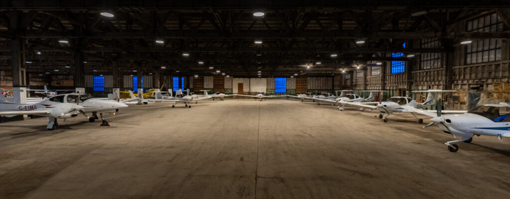 Wide interior view of an aircraft hangar with multiple small training planes parked side by side

