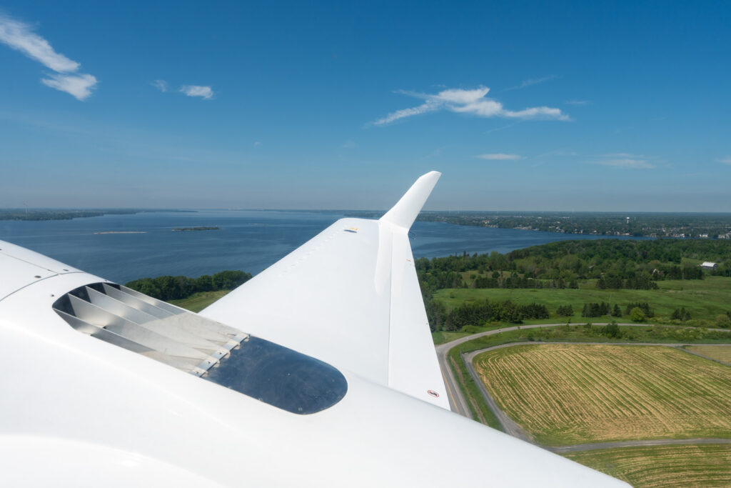 View airplane wing as it takes off with view of water and land in the background. 