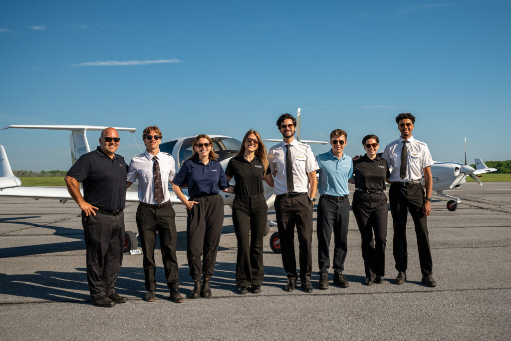 Eight students in front of an aircraft with blue skies on the runway.